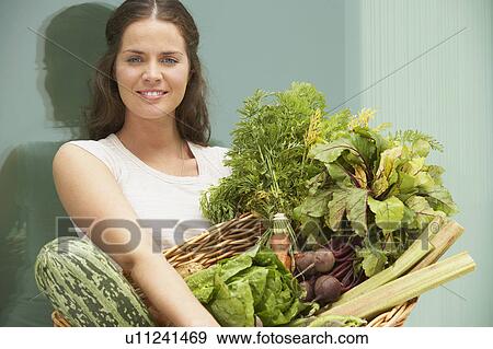 Stock Photo - Young woman with large basket of organic vegetables.. Fotosearch