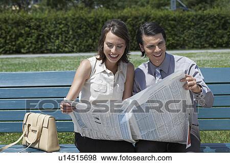 Businessman and woman on bench in park reading a newspaper together smiling. View Large Photo Image Stock Photo - Businessman and woman on bench in park reading a newspaper together smiling.. Fotosearch