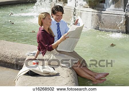 Businessman and woman sitting on fountain reading newspaper together laughing. View Large Photo Image Stock Image - Businessman and woman sitting on fountain reading newspaper together laughing.. Fotosearch