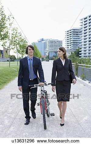 Businessman and woman walking in park he is walking his bike talking. View Large Photo Image Stock Photograph - Businessman and woman walking in park he is walking his bike talking.. Fotosearch