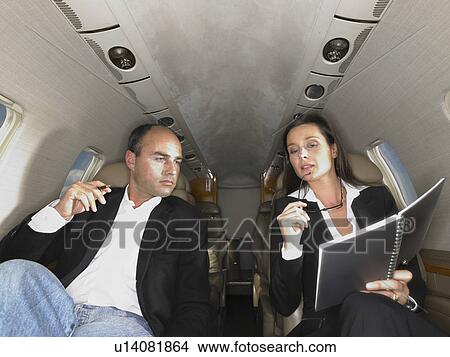 Businesswoman and businessman seated inside a private jet having a discussion. View Large Photo Image Picture - Businesswoman and businessman seated inside a private jet having a discussion.. Fotosearch
