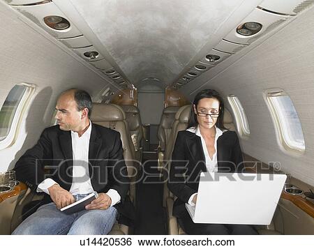 Stock Photograph - Businesswoman with a laptop and businessman seated inside a private jet.. Fotosearch