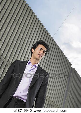 Stock Image - Low angle portrait of young man in suit by textured concrete wall, Alicante, Spain,. Fotosearch