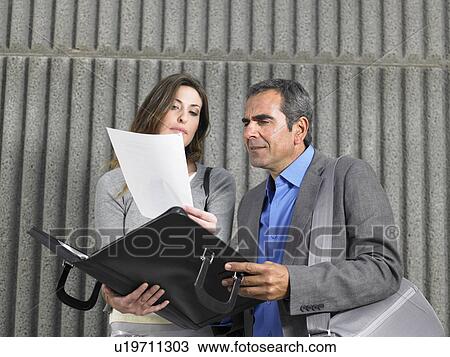 Stock Image - Older man and young woman reading paper from document case against textured concrete, Alicante, Spain,. Fotosearch