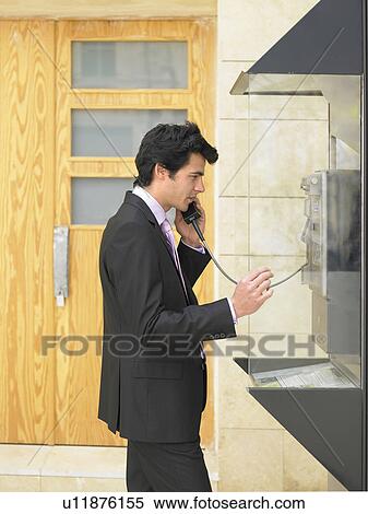 Stock Photography - Side view of young man in suit talking on public phone, Alicante, Spain,. Fotosearch
