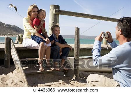 A family sitting on a beach, father taking picture View Large Photo Image Stock Photograph - A family sitting on a beach, father taking picture. Fotosearch