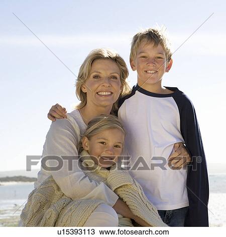 Stock Image - A mother and her children sitting on a beach. Fotosearch