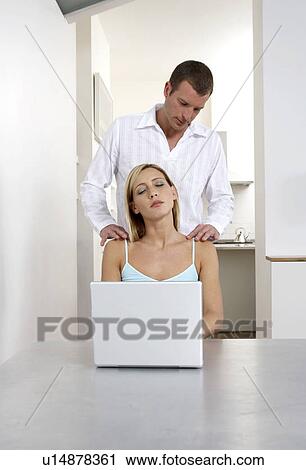Stock Image - Young woman receiving a shoulder massage whilst working from home. Fotosearch