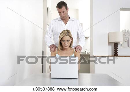 Stock Photo - Young woman receiving a shoulder massage whilst working from home. Fotosearch