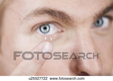 Stock Image - A young man inserting a contact lens. Fotosearch