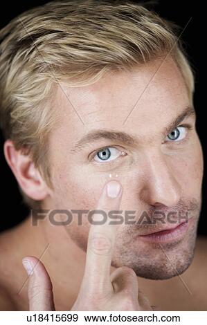 Stock Photo - A young man inserting a contact lens. Fotosearch