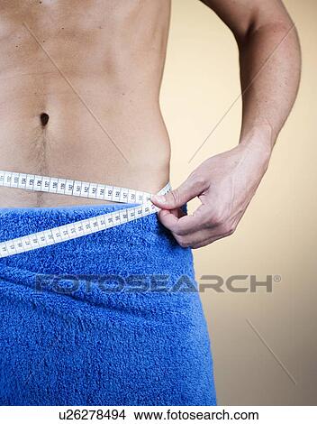 Picture - A young man measuring his waist. Fotosearch