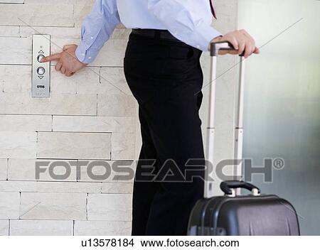 A businessman with a suitcase calling a lift View Large Photo Image Picture - A businessman with a suitcase calling a lift. Fotosearch