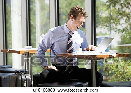 Stock Photo - A businessman working on a laptop computer in a hotel lobby. Fotosearch