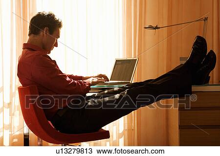 Stock Image - A man using a laptop at a desk. Fotosearch
