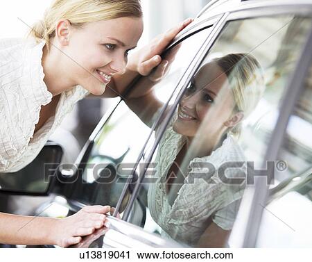 Stock Image - A young woman admiring a new car. Fotosearch