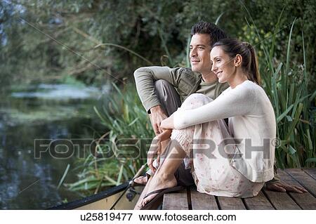 Young couple sitting by a river View Large Photo Image Stock Photo - Young couple sitting by a river. Fotosearch