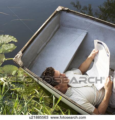 Young man laying in a boat reading a newspaper View Large Photo Image Stock Image - Young man laying in a boat reading a newspaper. Fotosearch