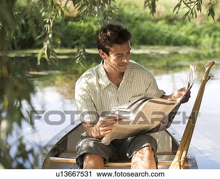 Stock Image - Young man sitting in a boat reading a newspaper. Fotosearch