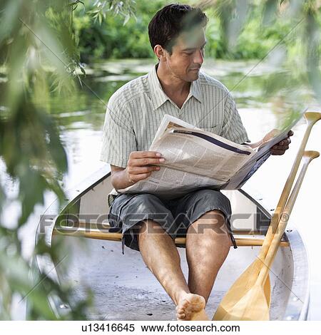 Stock Photography - Young man sitting in a boat reading a newspaper. Fotosearch
