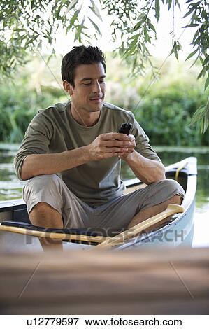 Young man sitting in a boat talking on a mobile phone View Large Photo Image Stock Photo - Young man sitting in a boat talking on a mobile phone. Fotosearch