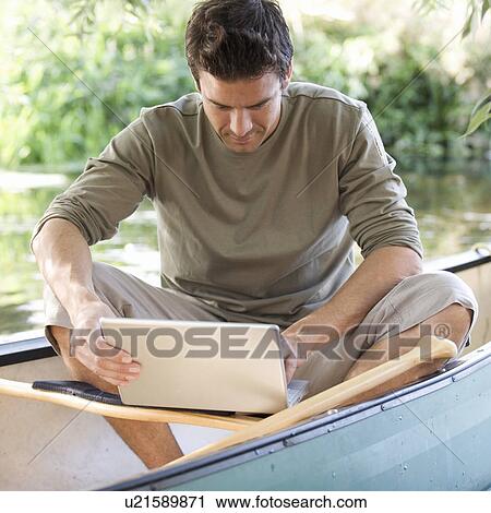 Young man sitting in a boat working on a laptop View Large Photo Image Stock Image - Young man sitting in a boat working on a laptop. Fotosearch