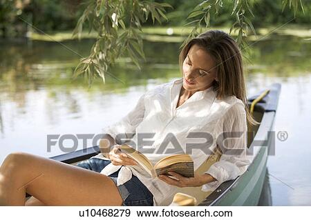 Stock Photo - Young woman sitting in a boat reading a book. Fotosearch