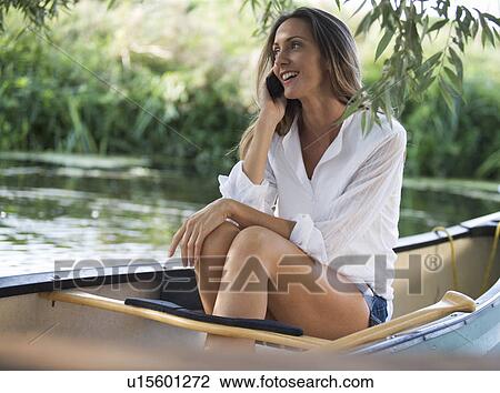 Stock Image - Young woman sitting in a boat talking on a mobile phone. Fotosearch
