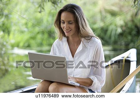 Stock Photo - Young woman sitting on a boat working on a laptop. Fotosearch