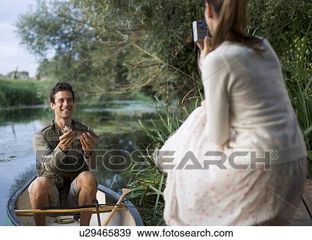 Young woman taking a photo of her partner's fishing success View Large Photo Image Stock Photo - Young woman taking a photo of her partner's fishing success. Fotosearch