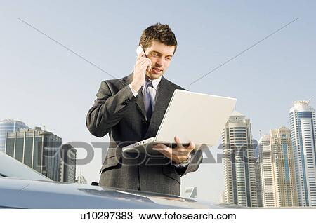 A businessman talkingon a mobile phone holding a laptop View Large Photo Image Stock Image - A businessman talkingon a mobile phone holding a laptop. Fotosearch