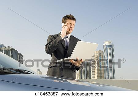A businessman talkingon a mobile phone holding a laptop View Large Photo Image Stock Photo - A businessman talkingon a mobile phone holding a laptop. Fotosearch