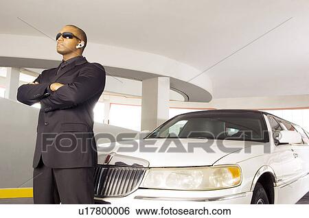 Stock Photograph - A chauffer standing by a stretch limousine. Fotosearch
