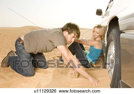Stock Photograph - A couple couple digging their car out of the sand. Fotosearch