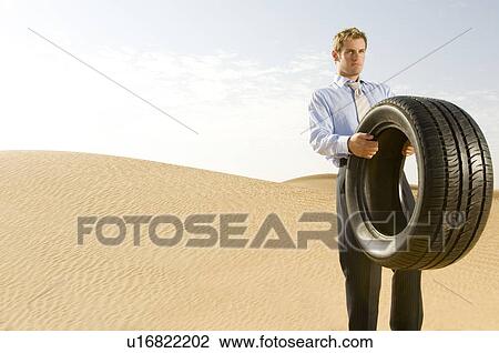 Stock Image - A man standing in the desert with a tyre. Fotosearch