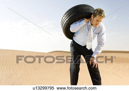 Stock Photography - A man standing in the desert with a tyre. Fotosearch