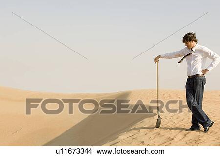 A young man standing in the desert with a spade View Large Photo Image Picture - A young man standing in the desert with a spade. Fotosearch