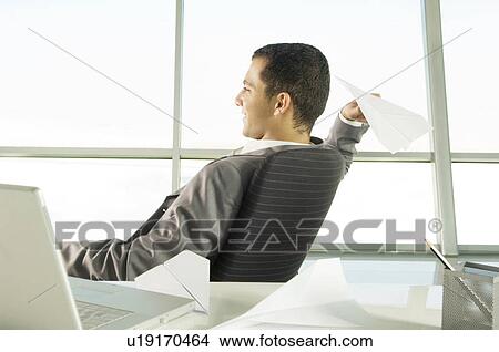 Picture - A businessman sitting at a desk making paper airplanes. Fotosearch