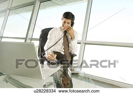 A businessman sitting at his desk talking on the telephone View Large Photo Image Picture - A businessman sitting at his desk talking on the telephone. Fotosearch