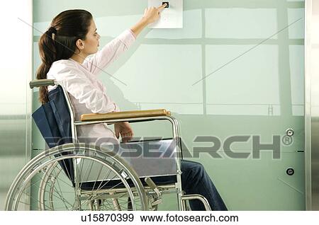 Stock Photo - A woman in a wheelchair pressing the button for a lift. Fotosearch