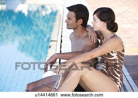 Stock Image - A young couple sitting by a swimming pool. Fotosearch