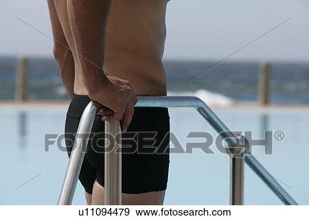 Stock Photo - A young man standing by a swimming pool. Fotosearch