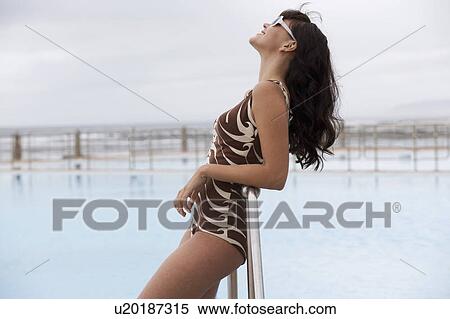 Stock Photography - A young woman standing by a swimming pool. Fotosearch