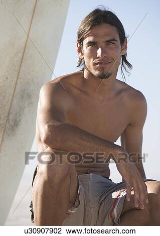 Stock Image - A surfer sitting on a beach. Fotosearch