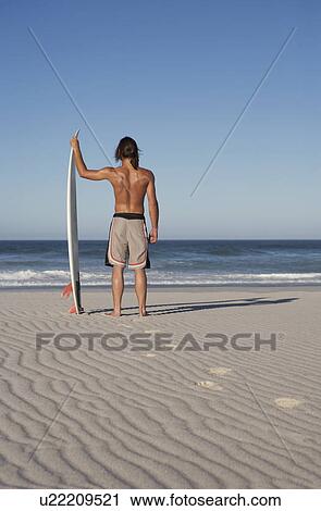A surfer standing on a beach View Large Photo Image Stock Image - A surfer standing on a beach. Fotosearch