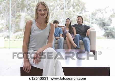 Stock Image - A mother sitting on a coffee table with her family sitting on a sofa. Fotosearch