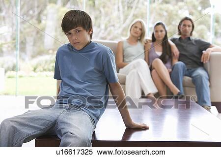 Stock Photography - A young boy sitting on a coffee table with his family on the sofa. Fotosearch