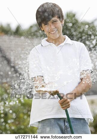 Picture - A young boy watering the garden with a hose. Fotosearch