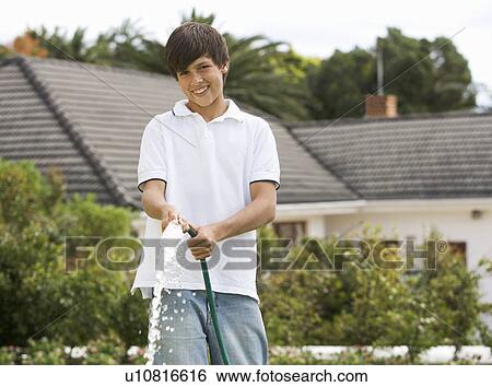 A young boy watering the garden with a hose View Large Photo Image Stock Photograph - A young boy watering the garden with a hose. Fotosearch