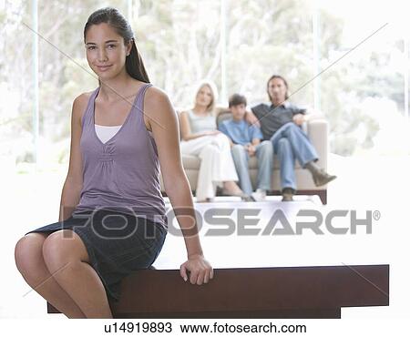 A young girl sitting on a coffee table with her family on the sofa View Large Photo Image Stock Image - A young girl sitting on a coffee table with her family on the sofa. Fotosearch